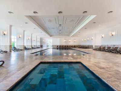 Piscine intérieure spacieuse avec jacuzzi au premier plan et chaises longues autour.