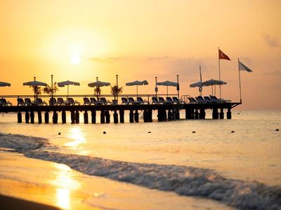 Coucher de soleil sur une plage avec un ponton et des parasols.