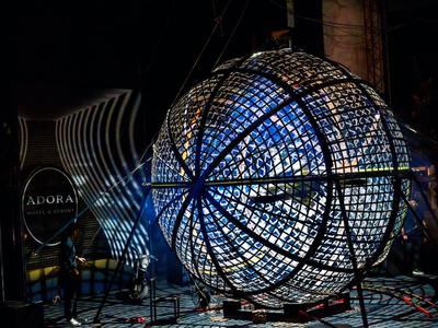 Grande installazione luminosa sferica con luci blu e bianche in una stanza buia