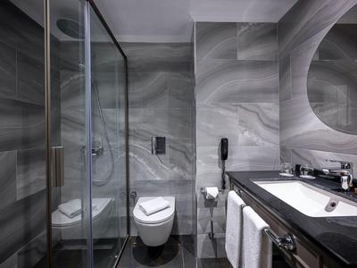 Salle de bain moderne avec douche vitrée, toilette suspendue et lavabo sous miroir rond.