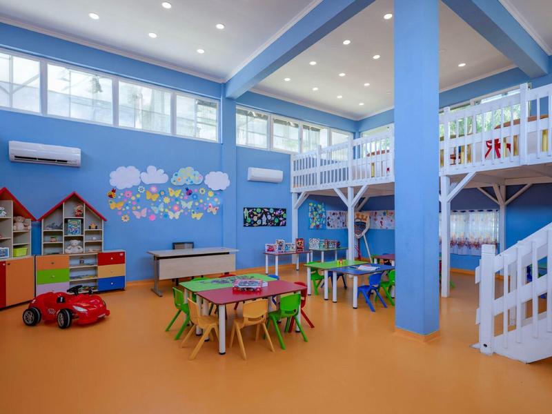 Salle de jeux colorée pour enfants avec tables, chaises, jouets et décoration murale.