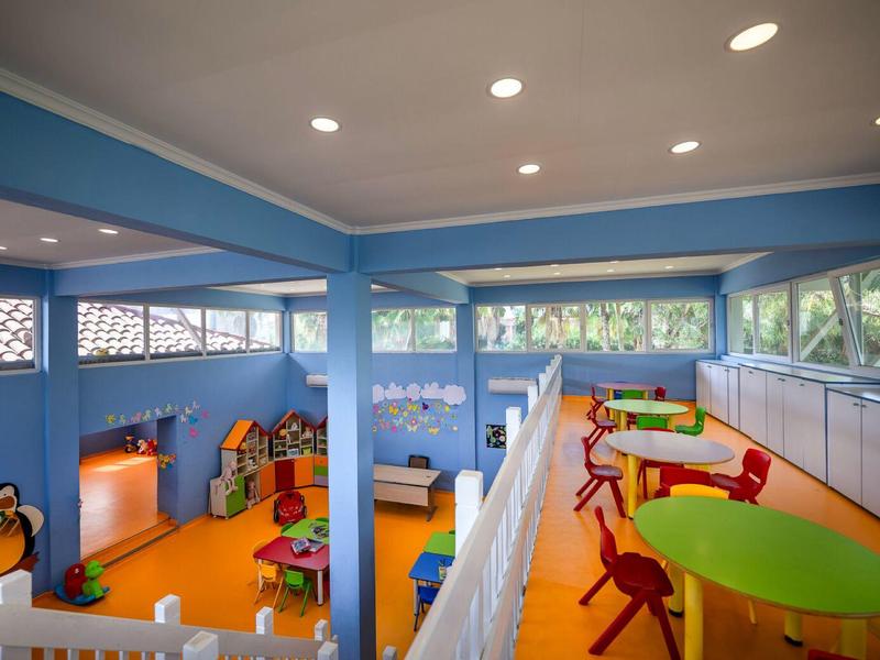 Espace enfants coloré avec tables, chaises, jouets et grandes fenêtres.