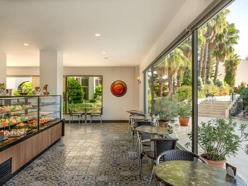 Salon lumineux avec tables, chaises et comptoir près d'une grande baie vitrée donnant sur un jardin.