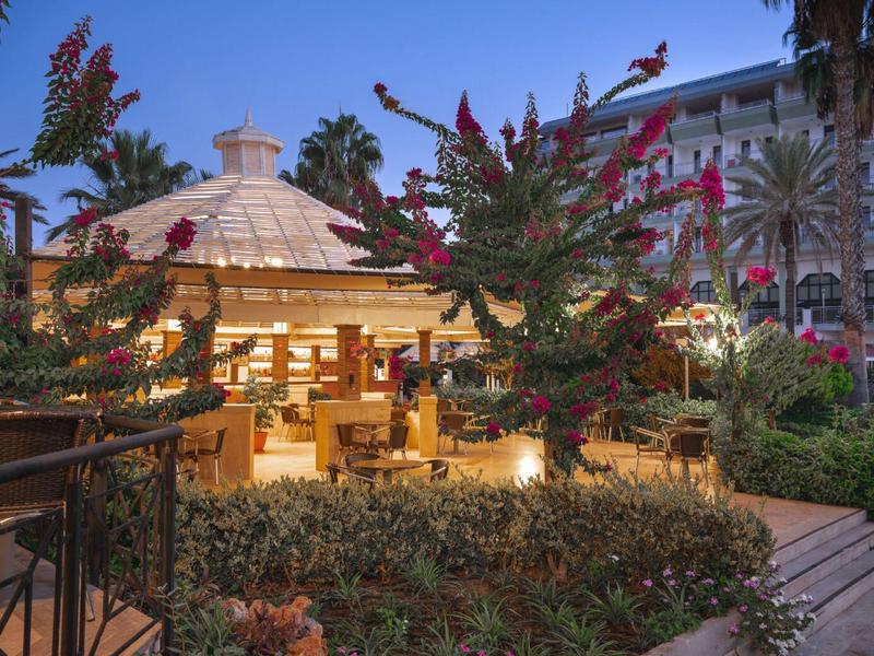 Restaurant extérieur chaleureux dans un jardin avec des fleurs et des palmiers en soirée.