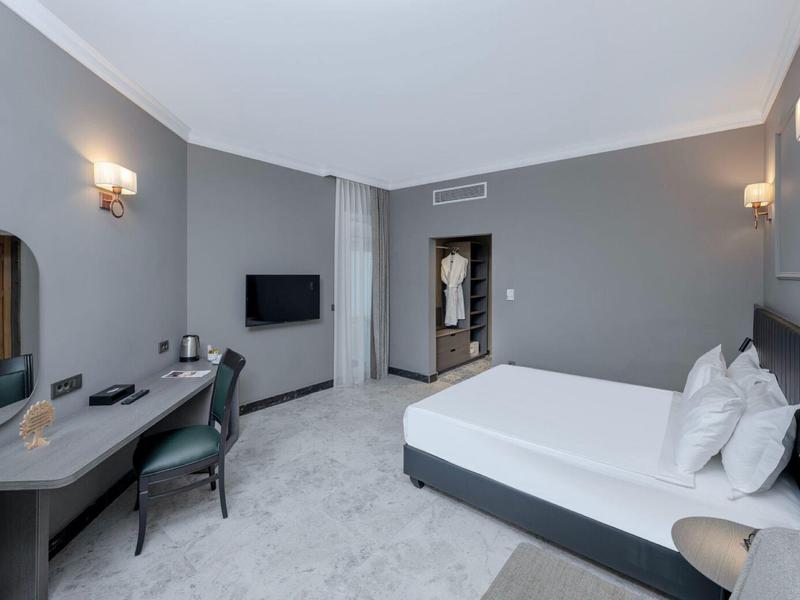 Chambre d'hôtel moderne avec lit double, bureau, TV murale et murs gris.