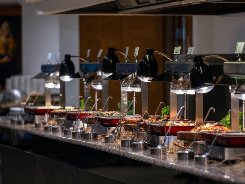 Buffet élégant avec plusieurs plats chauds sous des lampes chauffantes dans un hôtel.