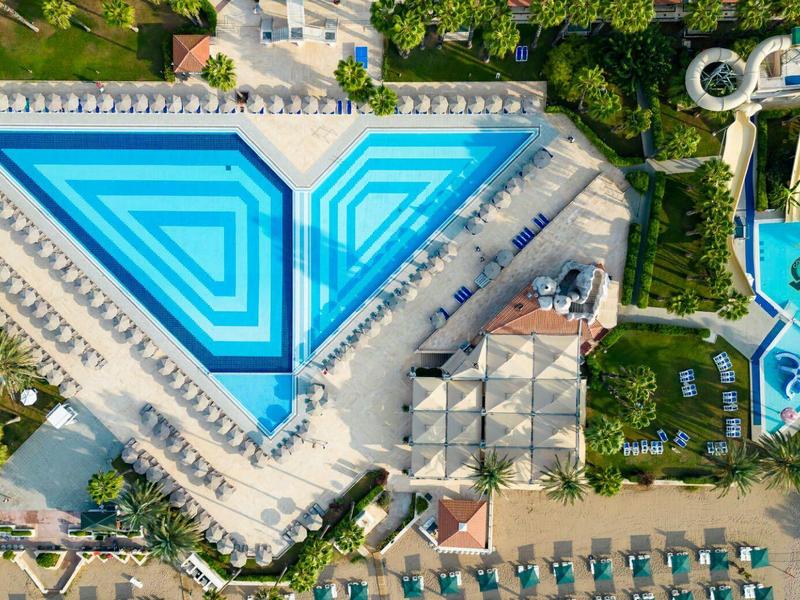 Grande piscine triangulaire et toboggans aquatiques dans un complexe hôtelier avec transats.