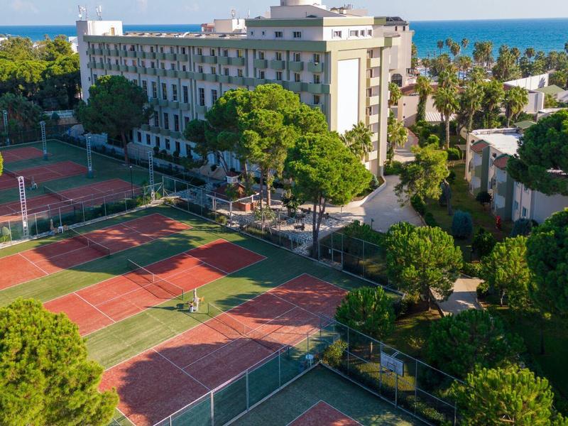 Hôtel avec plusieurs courts de tennis entourés d'arbres verts près de la mer.