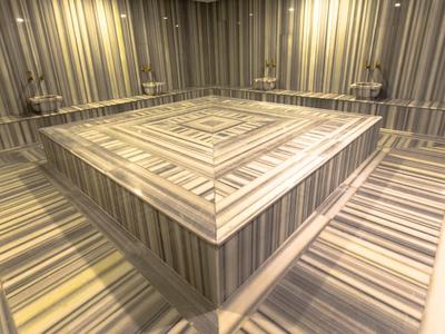 Moderně navržená místnost hammam s obdélníkovým vyhřívaným kamenem uprostřed a proužkovanými stěnami.