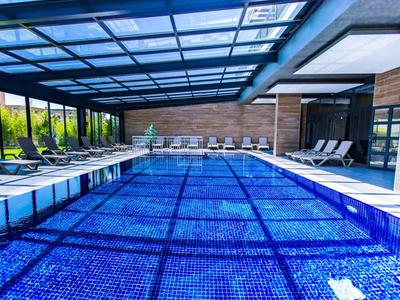Piscine intérieure moderne avec carrelage bleu, chaises longues et grandes fenêtres en verre