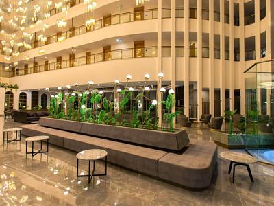 Hall d'hôtel moderne avec des bancs élégants, des tables et des plantes vertes au centre.