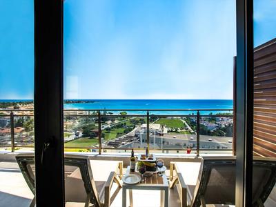 Balcon avec deux chaises et table avec vue sur la mer et la ville sous un ciel dégagé.