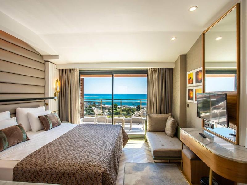 Chambre d'hôtel moderne avec lit double et vue sur la mer par de grandes baies vitrées.