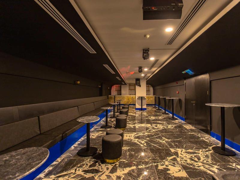 Espace lounge moderne avec long canapé, petites tables et sol à motif.