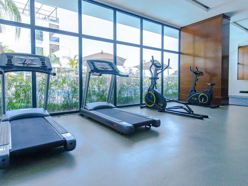 Salle de sport lumineuse avec tapis de course modernes et équipements devant de grandes fenêtres.