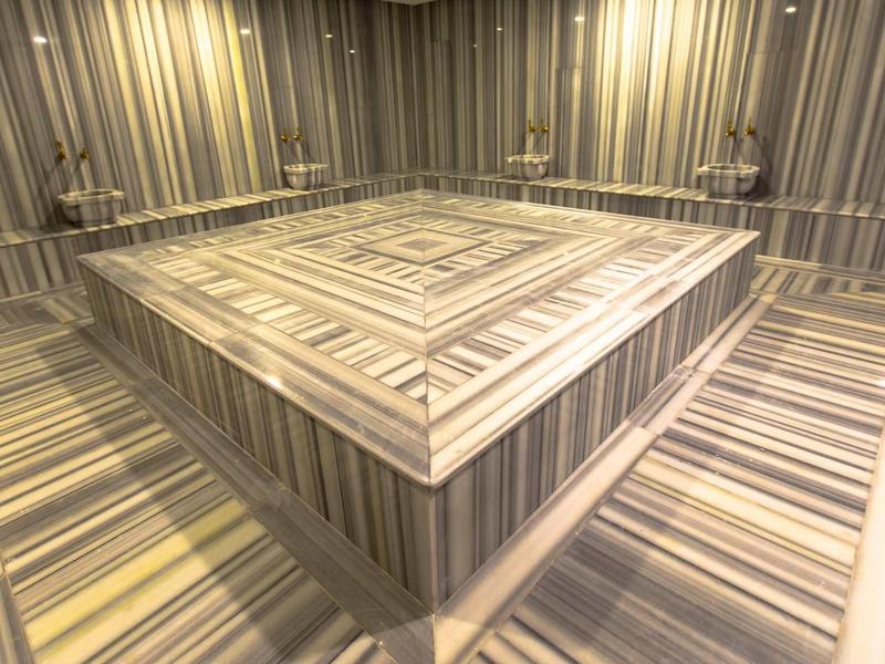 Hammam moderne avec une table carrée en marbre et des motifs rayés sur les murs et le sol.