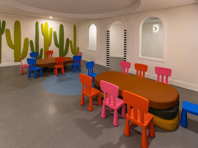 Espace de jeu coloré pour enfants avec table ronde et chaises devant un mur décoré de cactus.