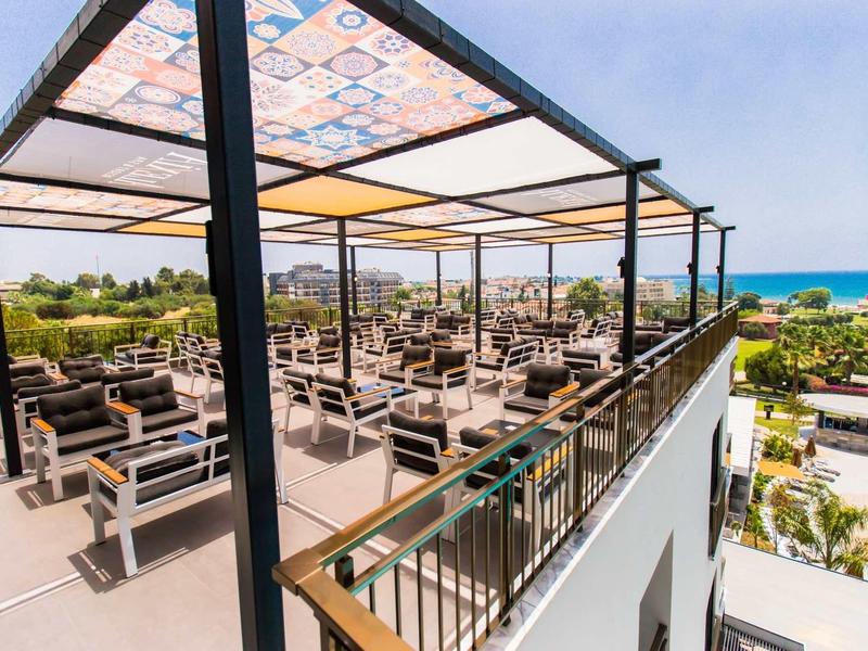 Terrasse sur le toit d'un hôtel avec des espaces de repos et vue sur la mer et les environs.