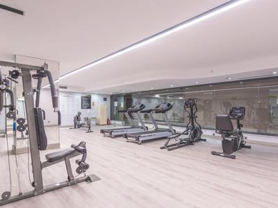 Moderne Fitnessraum mit verschiedenen Trainingsgeräten und hellem Bodenbelag.
