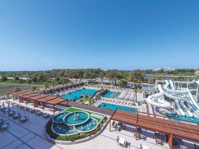 Velký bazén s tobogány, lehátky a zelení pod jasnou modrou oblohou.