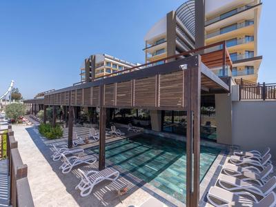 Terasa s bazénem a lehátky mezi moderními budovami pod modrou oblohou.