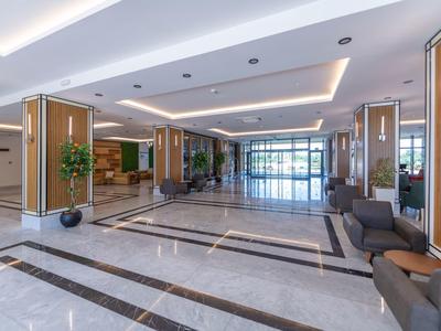 Prostorná vstupní hala se šedými pohovkami a světlými dřevěnými stěnami.