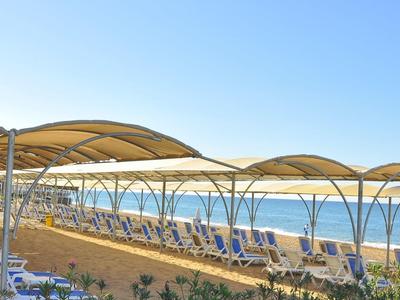 Pláž s řadami slunečníků a lehátek pod jasnou modrou oblohou.