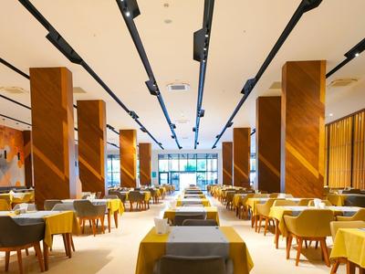 Velká elegantní restaurace s dřevěnými stoly, židlemi a množstvím přirozeného světla.