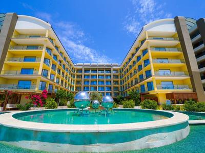 Moderní hotel s kulatým bazénem pod jasnou modrou oblohou.