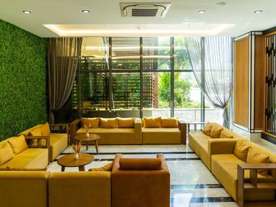 Světlý hotelový salonek se žlutými pohovkami, zelenými stěnami a velkými okny s výhledem na zahradu.