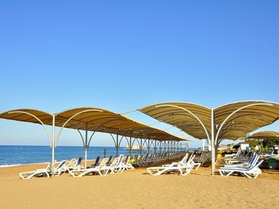 Bílé slunečníky a lehátka na písečné pláži pod jasně modrou oblohou.