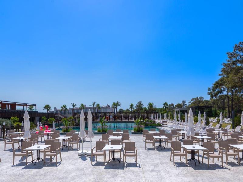 Prostranná terasa s mnoha stoly a slunečníky pod jasně modrou oblohou.