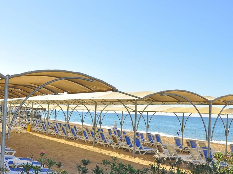 Pláž s řadami slunečníků a lehátek pod jasnou modrou oblohou.