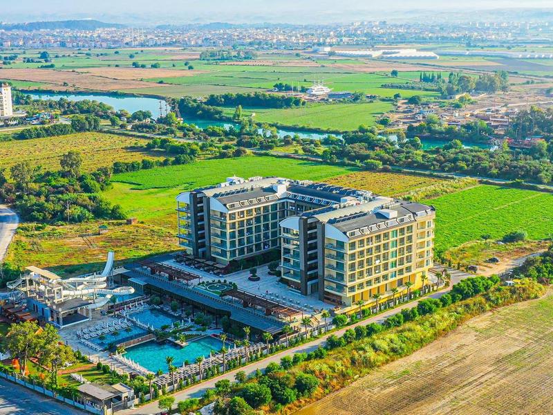 Letecký pohled na moderní hotel s bazénem obklopený zelenými poli a cestami.