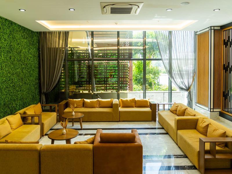 Světlý hotelový salonek se žlutými pohovkami, zelenými stěnami a velkými okny s výhledem na zahradu.