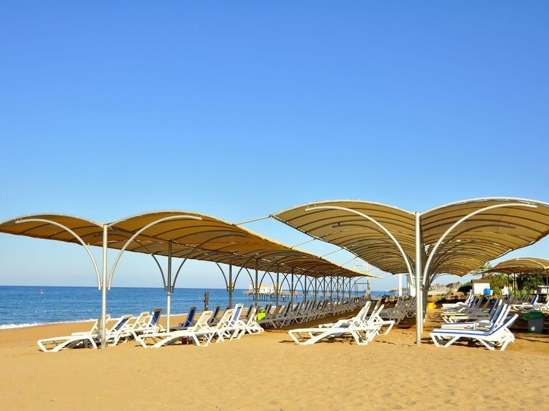 Bílé slunečníky a lehátka na písečné pláži pod jasně modrou oblohou.