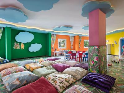 Buntes, gemütliches Spielzimmer mit Kissen, Tischen, Stühlen und Wolken an Decke und Wand.