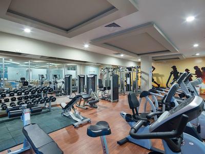 Modernes Fitnessstudio mit Hanteln, Krafttrainingsgeräten und Cardiogeräten in hellem Raum.