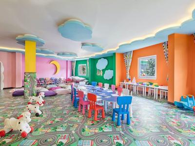 Bunter, großer Kinderraum mit Spielzeug, kleinen Tischen, Stühlen und regenbogenfarbener Dekoration.