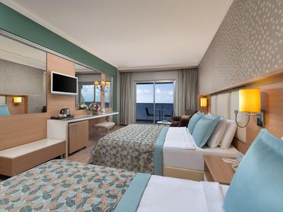 Habitación de hotel moderna con dos camas, escritorio y balcón con vista al mar.
