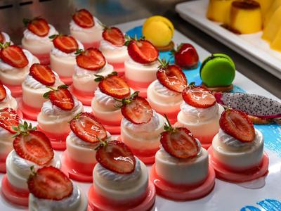 Varios pequeños postres blancos y rojos con fresas y macarons coloridos encima.