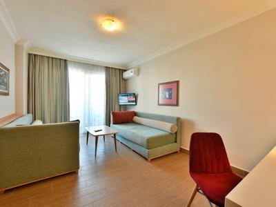 Área de sala luminosa en habitación de hotel con sofá, silla, escritorio y TV cerca de la ventana.