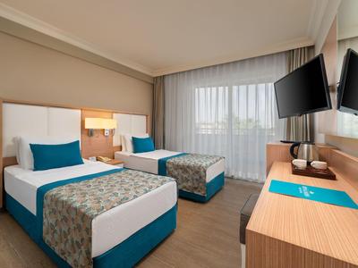 Habitación de hotel con dos camas individuales, paneles de madera y dos televisores en la pared junto a la ventana.