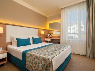 Habitación de hotel moderna con cama doble, mesas de noche y gran ventana con cortinas.