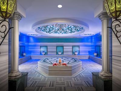 Spa lujoso con cuenca de agua central, piso de mosaico y luz suave.