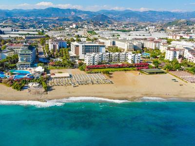 Vista de un complejo hotelero en la playa con agua turquesa y montañas al fondo.