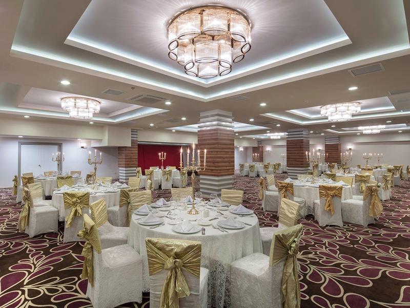 Elegante banket zaal met ronde tafels en witte-gouden stoelhoezen.