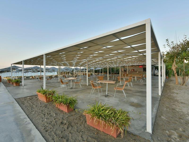 Overdekt buitengebied met tafels en stoelen naast een strand.