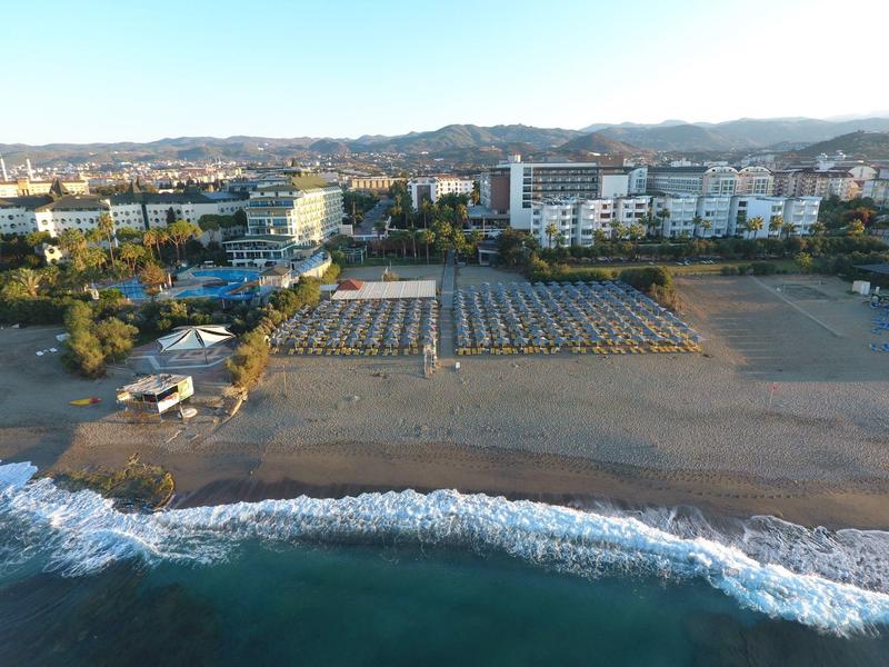 Strand met rijen parasols en ligstoelen voor een stad met gebouwen en bergen op de achtergrond.