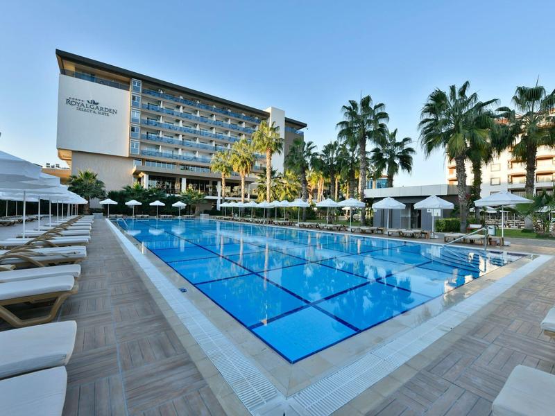 Modern hotelzwembad met ligstoelen en palmbomen onder een heldere hemel.